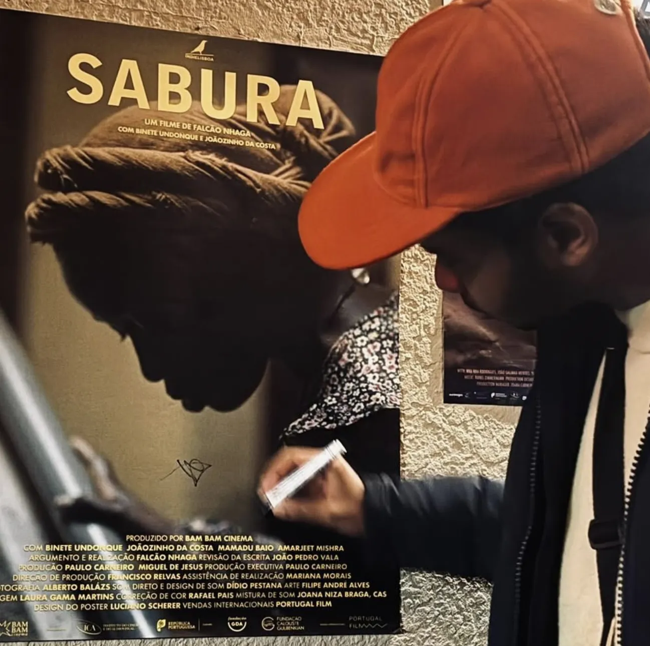 Falcão Nhaga signiert das Plakat von Sabura